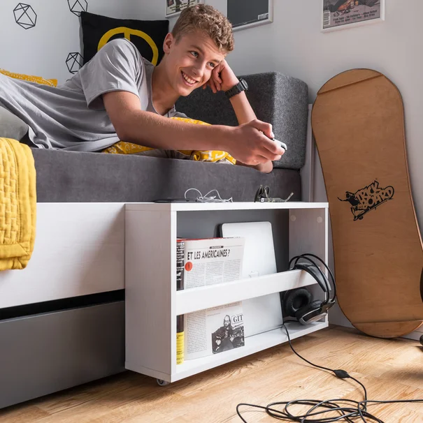 nastolatek leżący na łóżku z półką na gazety, laptopa i słuchawkami